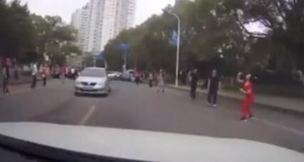 哭笑不得!横跨马路打羽毛球太惊险 汽车从球下穿行